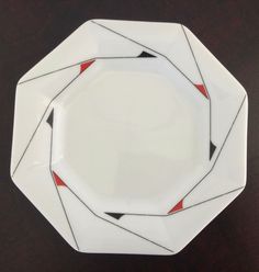 a white plate with red and black designs on it sitting on a wooden table top