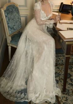 a woman sitting at a desk wearing a white dress and holding a pen in her hand