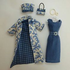 a doll's clothes and accessories are laid out on a table top, including a blue dress with white polka dots