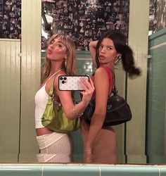 two beautiful women standing in front of a mirror taking a selfie with a cell phone