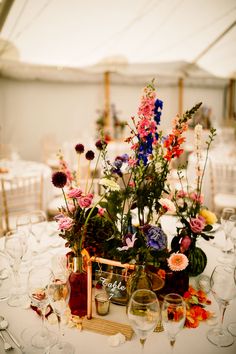 an arrangement of flowers and wine glasses on a table in a marquee at a wedding