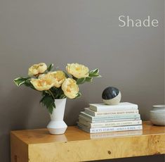 some yellow flowers are in a white vase on a wooden table next to books and a black rock