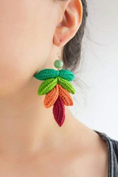 a close up of a person wearing earrings with crochet leaves on it and beads hanging from them