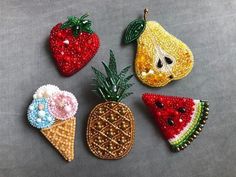 four pieces of beaded fruit and ice cream on a gray surface, each with different designs