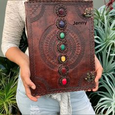 a woman is holding a leather journal with buttons and stones on the cover in front of plants