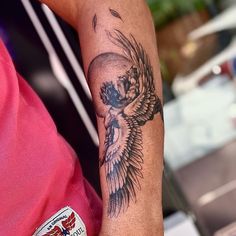 a person with a skull and wings tattoo on their arm, holding onto a cell phone