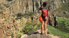 a woman standing on top of a rock next to a lush green valley filled with trees