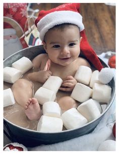 a baby in a santa hat sitting in a tub filled with marshmallows