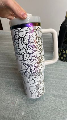 a hand holding a white coffee cup with floral designs on the front and sides,