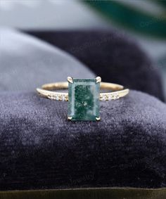 a ring with a green stone surrounded by white diamonds on top of a velvet cushion