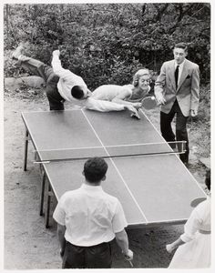 people playing ping pong in an old black and white photo with one man falling over the table