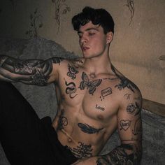 a man with tattoos on his chest and arm sitting on a couch next to a wall