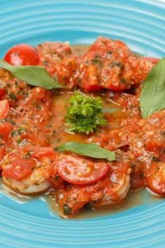 a blue plate topped with shrimp covered in tomato sauce and garnished with green leaves