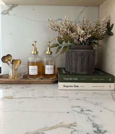 two bottles of liquid sitting on top of a counter next to some books and flowers