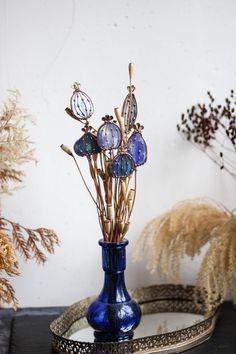 a blue vase filled with flowers sitting on top of a black table next to dried plants