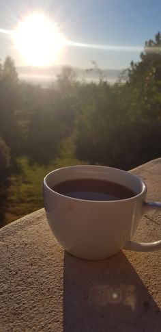 a cup of coffee sitting on top of a table next to the sun in the background