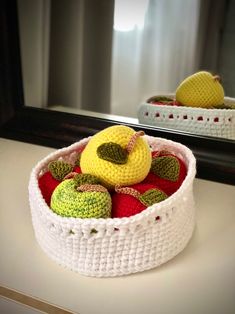 a crocheted basket filled with fruit sitting on top of a counter next to a mirror