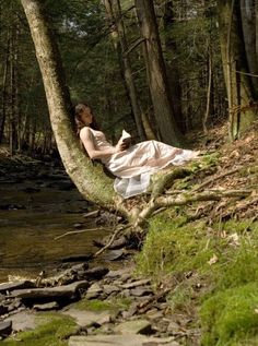 a woman sitting on top of a tree next to a river in the woods with words written