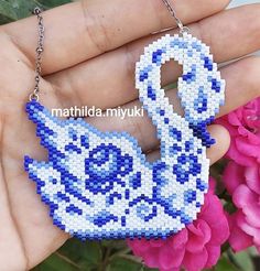 a hand holding a blue and white beaded swan ornament with flowers in the background