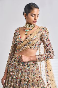 This antique gold net lehenga set has a dense sprinkling of all jewel tones of embroidery material - emerald, ruby, turquoise, gold, silver, pearl etc. It comes with a full sleeves blouse which has delicate tasselling at the sleeve hem and at the waist. The dupatta has four-sided border and dense sprinkling.From Seema Gujral’s Samode collectionDELIVERY TIMEPlease wait 8-12 weeks for your outfit to arrive.FABRIC DETAILSNetProfessional cleaning only. Elegant Pre-draped Kundan Saree For Party, Gold Pre-draped Saree For Reception, Festive Gold Embellished Pre-draped Saree, Transitional Bollywood Style Embellished Pre-draped Saree, Festive Hand Embellished Saree Sets, Diwali Hand Embellished Kundan Lehenga, Embellished Long Sleeve Pre-draped Saree For Party, Festive Hand Embellished Sharara For Navratri, Gold Hand Embellished Lehenga For Wedding