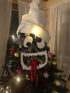 a decorated christmas tree with an evil face on it's head and lights in the background