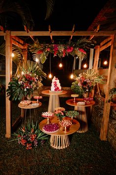 a table topped with cakes and flowers on top of a lush green field at night