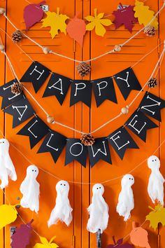 an orange door decorated for halloween with white ghostes and black happy halloween banner on it