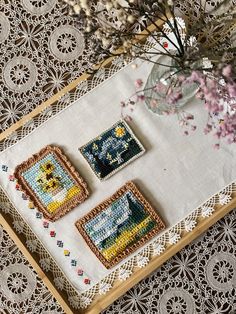 three cross stitch coasters sitting on top of a table next to a vase with flowers