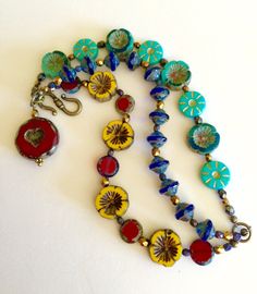 "Colorful bohemian style Czech glass multi strand flower bracelet with vintage bronze clasp and large Czech glass red heart bead charm. Bracelet is made of three separate but attached beaded strands of gorgeous Czech glass beads including: Sunflower yellow Picasso chunky pansy Cobalt blue Picasso UFO beads Turquoise/teal opaque gilded gold daisy coin beads Turquoise Hawaiian flower coral/teal/ turquoise beads Red Czech lentil beads Metallic bronze Czech fire polished faceted beads Gunmetal Czech Bohemian Red Bracelets Made Of Czech Glass, Bohemian Red Czech Glass Bracelets, Red Flower-shaped Bohemian Beaded Bracelets, Red Bohemian Flower Beaded Bracelets, Bohemian Red Flower Bracelets, Bohemian Red Flower Beaded Bracelet, Bohemian Jewelry With Heart Beads In Flower Shape, Bohemian Glass Jewelry With Heart Beads, Bohemian Red Heart-shaped Bracelet