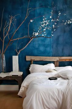 a bed with white sheets and pillows in a room decorated with blue walls, branches and flowers