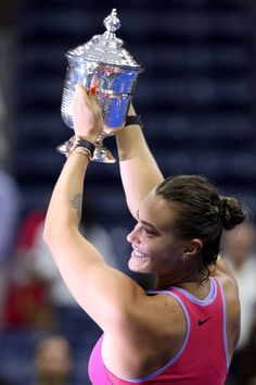 a woman holding up a trophy in the air with her arm above her head while wearing a pink tank top