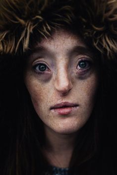 a woman with freckled hair and blue eyes looks into the camera while wearing a fur hat