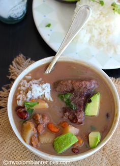 a bowl of soup with meat, rice and veggies on a table next to a plate