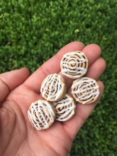 four small cookies with white icing in someone's hand on some green grass