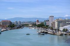 boats are parked along the river in front of some buildings and tall buildings with mountains in the background