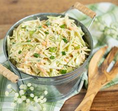 a bowl of coleslaw sits on a table next to two wooden utensils