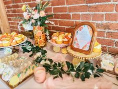 a table topped with cakes and pastries next to a brick wall covered in greenery