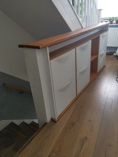 an empty room with wooden floors and white cupboards on the bottom floor, next to a stair case