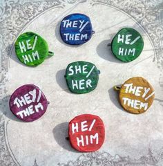 six different colored buttons with the words hey, him and she written on them in various languages