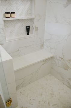 a bathroom with white marble walls and flooring next to a shelf on the wall