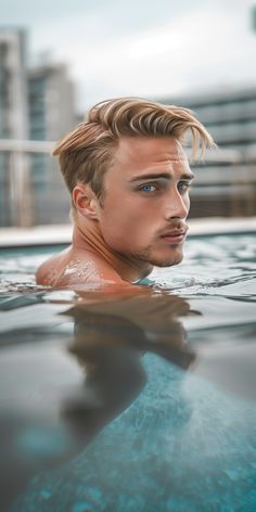 a young man is swimming in the pool with his hair blowing back and looking at the camera