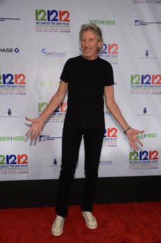 an older man standing on a red carpet in front of a white backdrop with his hands out