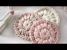 three crocheted coasters sitting on top of a white surface next to a brush