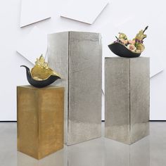 two metal sculptures sitting on top of blocks in front of a white wall with geometric shapes