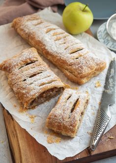 two pastries sitting on top of a cutting board next to an apple and knife