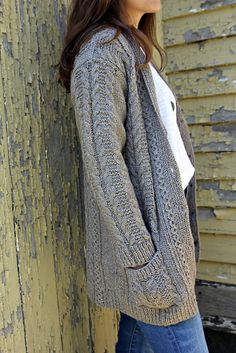 a woman leaning against a wall with her hands in her pockets