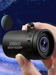 a hand holding a black camera in front of the space with planets and stars behind it