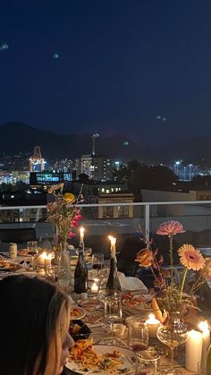 people are sitting at a table with food and drinks on it, overlooking the city lights