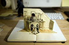 an open book with a cut out of a person sitting at a desk in front of a computer