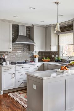 a kitchen with gray cabinets and white counter tops, an island in the middle is surrounded by hanging lights